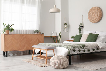 Interior of light bedroom with cozy bed, wooden cabinet and hanging houseplants