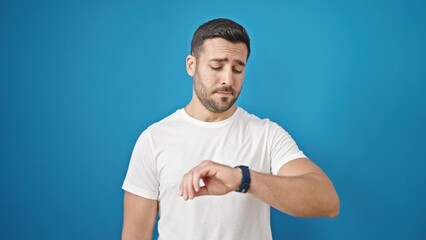 Poster - Young hispanic man looking watch with relaxed expression over isolated blue background