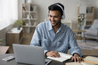 © fizkes - Cheerful young adult Indian student guy in headphones watching learning video on laptop, talking on video call to teacher, studying online, using Internet technology for education