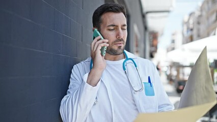 Poster - Young hispanic man doctor reading medical report talking on smartphone at hospital