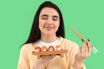 Canvas Print - Happy young woman with sushi and chopsticks on green background