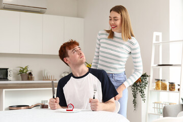 Wall Mural - Young woman proposing to her upset boyfriend at table in kitchen