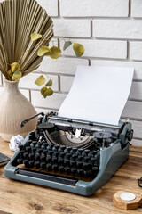 Wall Mural - Vintage typewriter with candle and vase of dry palm leaf on brown wooden table near brick wall