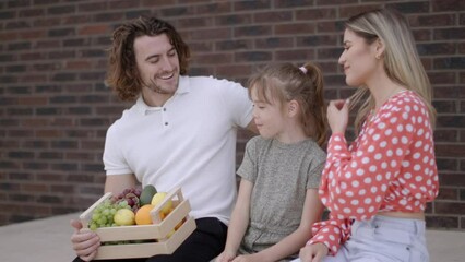 Wall Mural - Family with a mother, father and daughter sitting outside on steps of a front porch of a brick house and eating fresh fruits