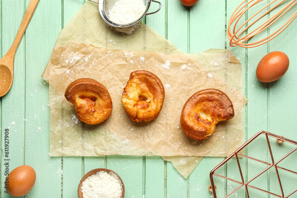 Tasty Yorkshire pudding and ingredients on green wooden background