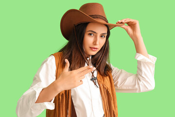 Poster - Beautiful cowgirl showing gun gesture on green background