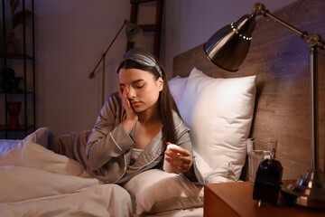 Canvas Print - Young woman taking pill bottle in bedroom at night