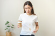 Cloth stain, disappointment asian young woman clumsy with hot coffee, tea stains on shirt, hand show making spill drop on white t-shirt, spot dirty or smudge on clothes at home, isolated on background