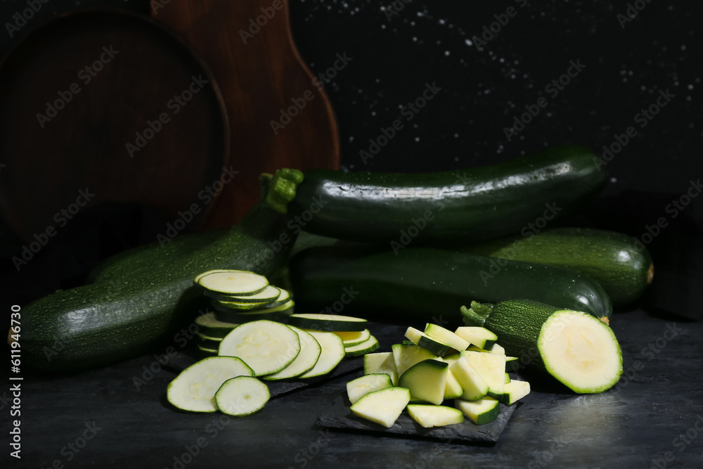 Many fresh zucchini and slices on black background