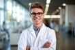 © igolaizola - Portrait of smiling young male doctor standing with arms crossed in hospital