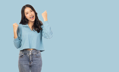 Wall Mural - Excited young asian female with raised hands celebrating success Portrait cheerful positive asian woman with raised hands and fists open mouth Girl get happy Pastel blue background, copy space