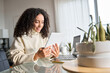 © insta_photos - Young happy latin woman, curly casual girl student using digital tablet and laptop elearning or remote hybrid working at home online looking at tab technology device sitting at table in living room.