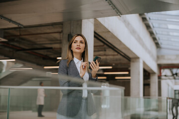 Wall Mural - Young business woman using mobile phone in the office hallway