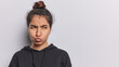 Horizontal shot of displeased dark haired young Latin woman pouts lips and frowns face dressed in casual black sweatshirt isolated over white background copy space for your advertising content