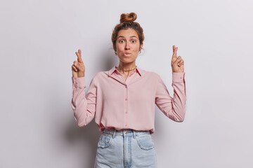 Wall Mural - Lovely young European woman stands with anticipation her finger crossed and hopeful smile on face exudes sense of belief in positive outcomes has desire for good fortune dressed in elegant clothes