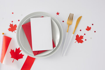 Wall Mural - Canada Day-themed table decor. Top view flat lay of canadian flag, plates, envelope with blank card, cutlery, maple leaves, red stars on white background