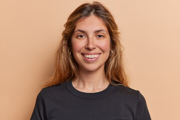 Poster - Portrait of lovely long haired woman smiles broadly shows white teeth has piercing in nose dressed in casual black t shirt isolated over brown background expresses positive emotions. Happiness concept