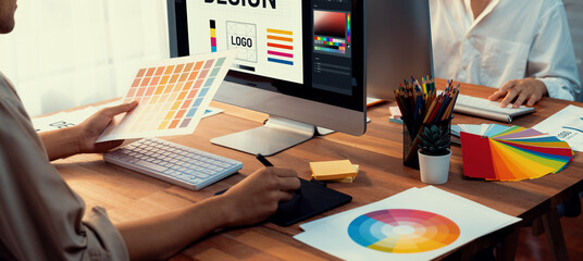 Poster - Graphic designer work on computer laptop and with graphic drawing pen while brainstorming unique design with professional graphic team in modern digital studio workplace. Panorama shot. Scrutinize