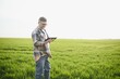 © Serhii - A young farmer inspects the quality of wheat sprouts in the field. The concept of agriculture.