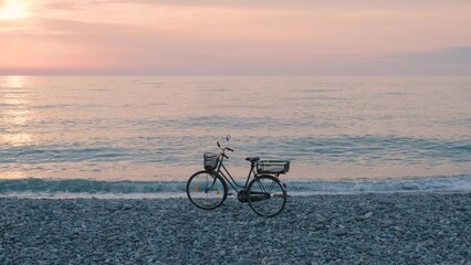 Wall Mural - Bicycle on the sea coast at sunset. Bike standing on the beach by the ocean. Minimal summer sunset seascape