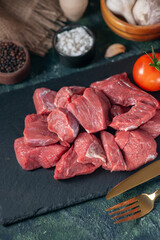 Close up view of fresh raw chopped meats and cutlery set tomatoes on wooden board garlics spices on dark background