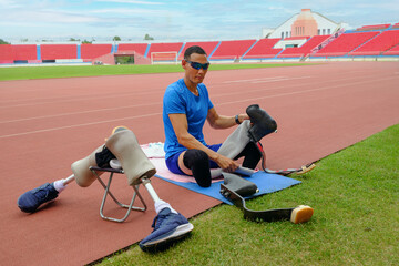 Wall Mural - portrait of an Asian paralympic athlete, seated on a stadium track, busily affixing his running blades, preparing for intense training