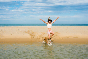 Beautiful fashionable young girl having fun on the beach barefoot with her dog