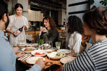 Waitress pouring wine into glasses while serving group of friends in restaurant