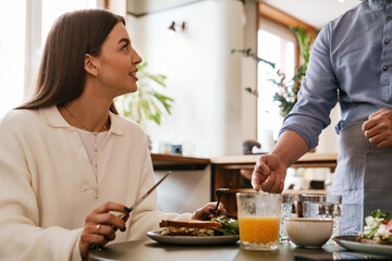 Wall Mural - Young woman talking with waiter while having lunch in cafe