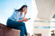 © Westend61 - Happy businesswoman holding smart phone sitting on bench
