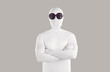 Portrait of person in bodysuit disguise and sunglasses. Man with secret, hidden personality, wearing white spandex costume and black round glasses standing with folded arms on grey color background