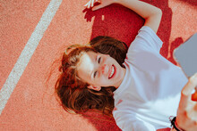 Cheerful Teenage Girl With Smart Phone Lying On Ground
