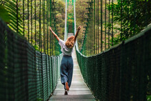Carefree Woman With Arms Raised Spending Leisure Time Walking On Suspension Bridge