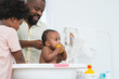 © Pruksachat - African middle aged father bathing adorable newborn baby daughter in bathtub at home. Son help dad cleaning little sister. Selective focus on little girl biting duck toy. Child hygiene and health care
