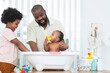 © Pruksachat - African middle aged father bathing adorable newborn baby daughter in bathtub at home. Child boy help dad cleaning and playing toy with little sister. Kid hygiene and health care with happy family