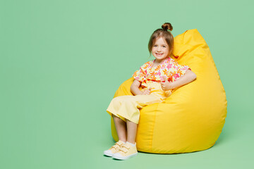 Wall Mural - Full body little child kid girl 6-7 years old wear casual clothes sit in bag chair show thumb up isolated on plain pastel green background studio portrait. Mother's Day love family lifestyle concept.