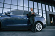 © standret - Holding smartphone. Businessman is standing near his car outdoors