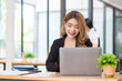 © wattana - Charming young businesswoman sitting in modern office and working on laptop computer.