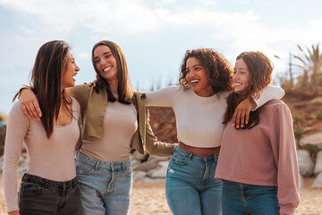 Wall Mural - Four multiracial girls hugging on beach.