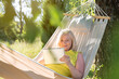 Senior woman using digital tablet and relaxing in summer hammock