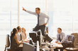 © KOTO - Laughing colleagues watching exuberant businessman dancing on top of desks in office