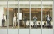 © KOTO - Business people talking on cell phones reviewing paperwork at conference room window