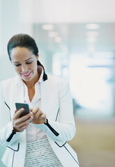 Wall Mural - Smiling businesswoman using cell phone in office corridor