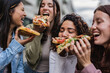 © PintoArt - Cheerful multiracial women eating pizza on the street - Happy millennial female friends enjoying weekend together while visiting an Italian city -