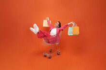 Happy Smiling Fashionable Woman With Trolley And Shopping Bags Walking Shopping Promotion Summer Sale Isolated On Orange Background.