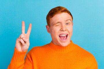 Happy positive teenager showing v sign to camera winking smiling young man wishing good luck isolated blue background