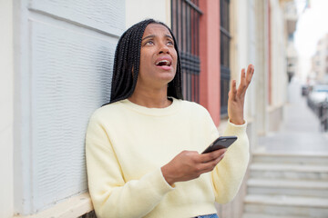 black afro woman screaming with hands up in the air. using a smartphone concept