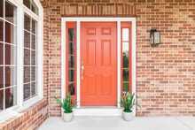 A Home's Red Front Door Surrounded By Red Brick And Plants Sitting In Front Of The Windows.