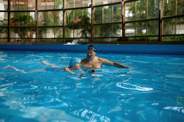 Wall Mural - Senior man instructor teaching young woman to swim at indoor pool