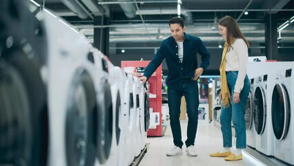 Wall Mural - Multicultural Couple Evaluates Washing Machine Choices at Home Electronics Store. Man and Woman in Search of a Reliable Laundry Appliance. Customers Explore Modern Laundry Solutions in a Retail Shop